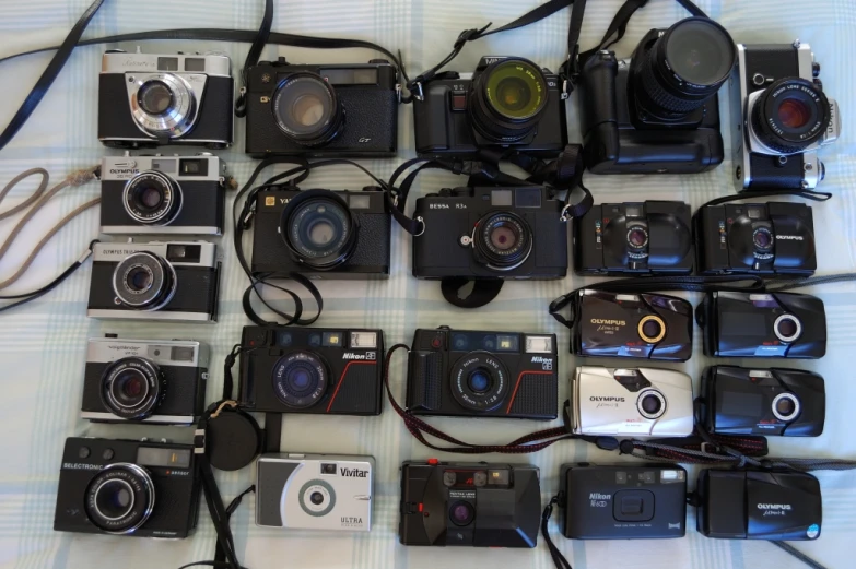 many cameras and lenses laid out on a bed