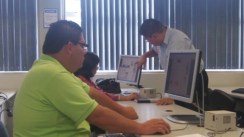 two men and a woman sitting in front of a computer monitor