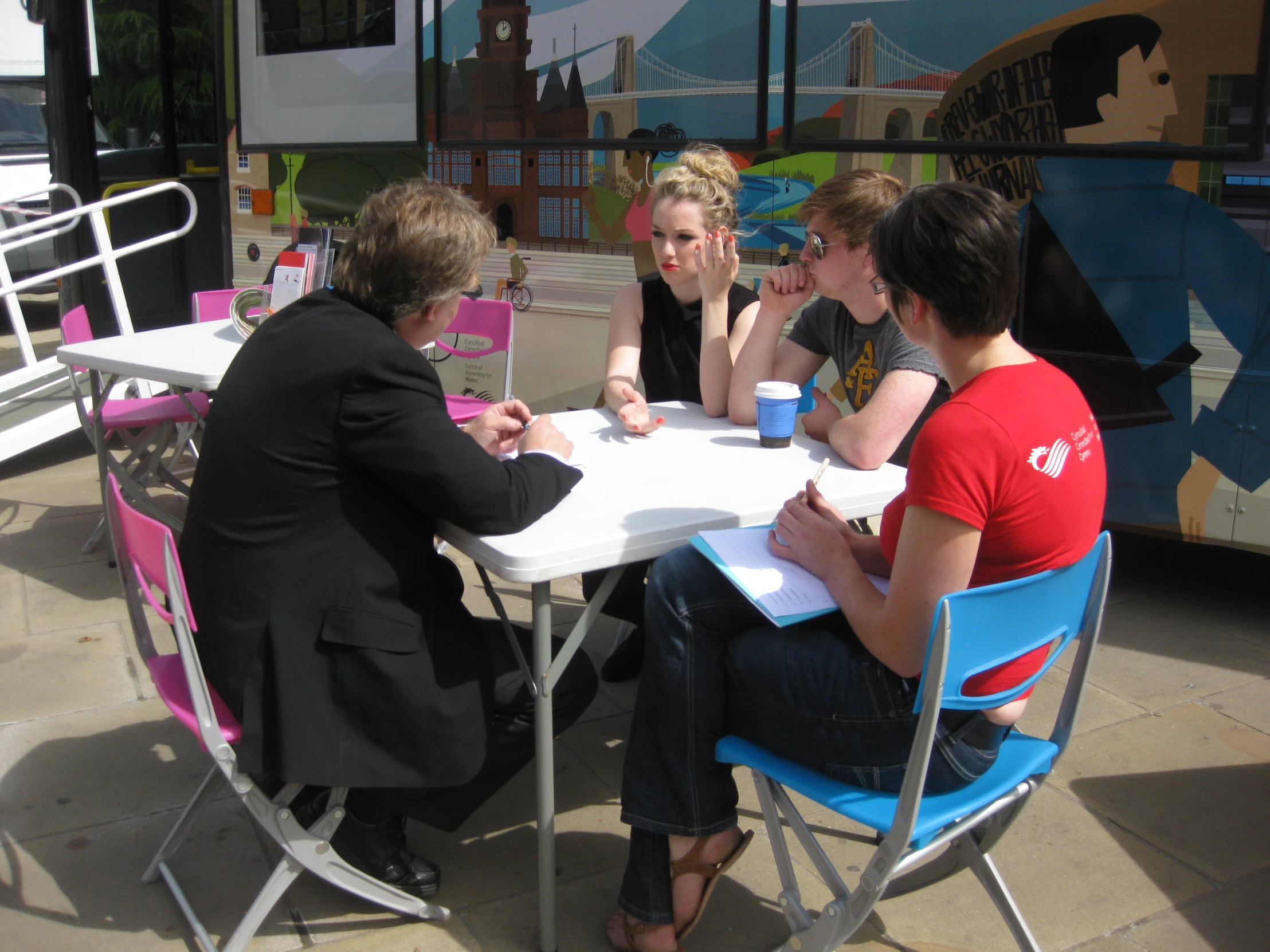 four people sitting at a table with cups of coffee in front of a bus