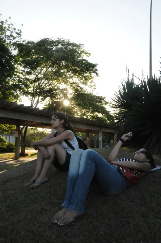 two girls sit on the grass one in high heels and the other down