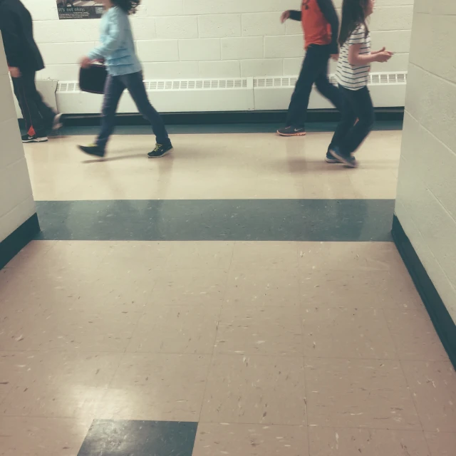 several people walking in a hallway next to white walls