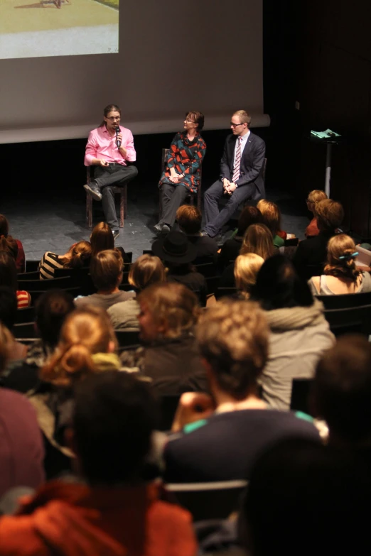 there are three people on the stage and one person sitting down