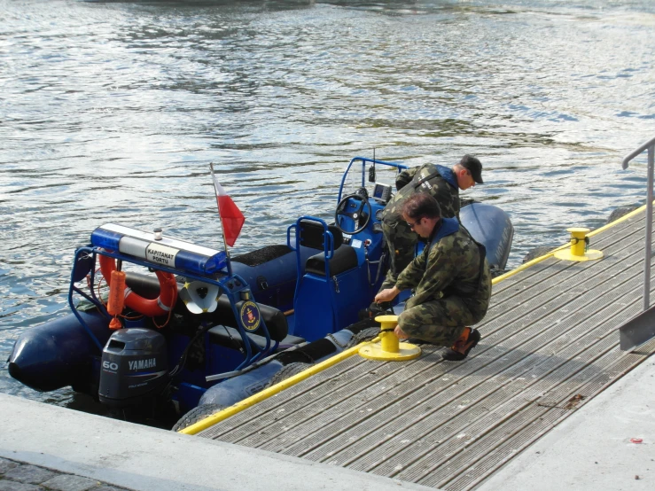 two men preparing a small blue boat on a body of water