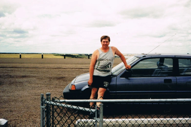 young man sitting on the hood of his car holding a surfboard