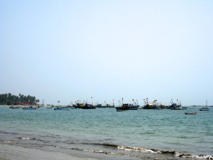 several boats floating on the ocean with people walking in the water