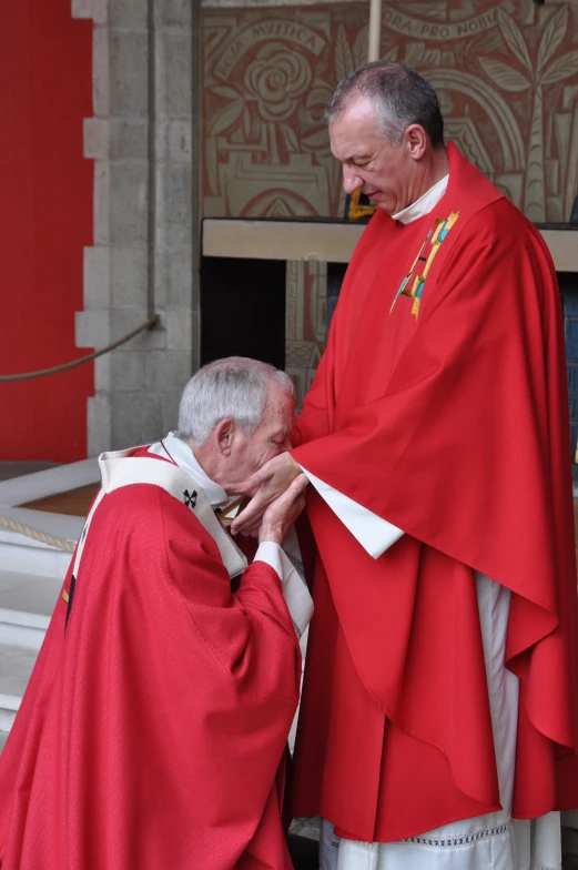 a man in a red priest outfit is shaking the hand of an older man