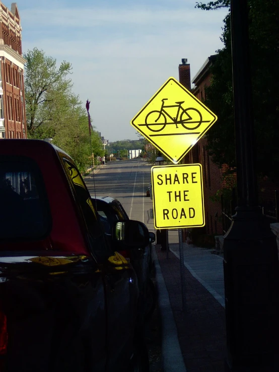 a yellow sign that says share the road next to two cars