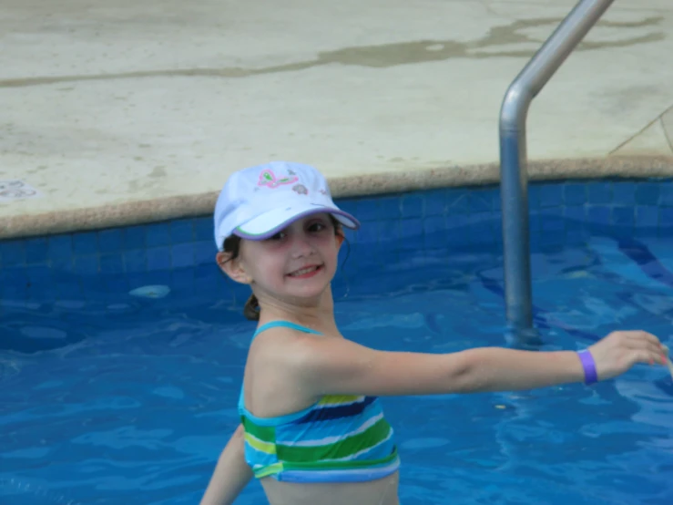 a girl in a swimming pool smiling wearing a hat