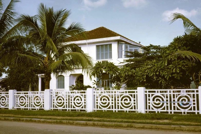 a white fence surrounding a house with palm trees in front of it