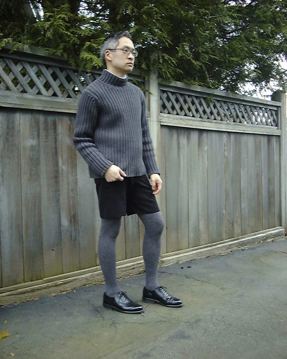 a man with black hair is wearing grey turtleneck and black shorts