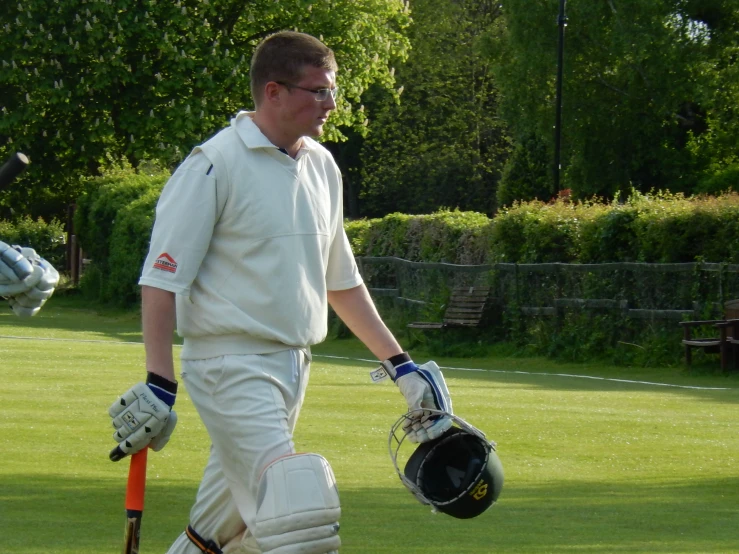 a person in white uniform walking across grass holding a bat