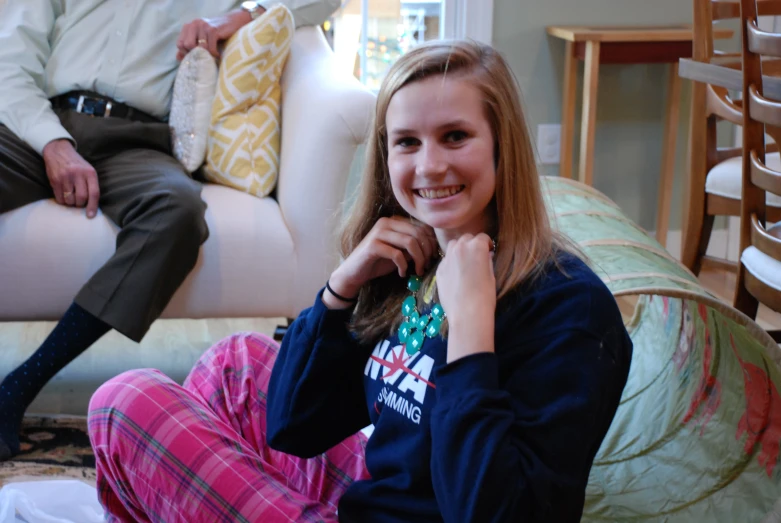 a woman with a blue sweater smiles while sitting on a white couch