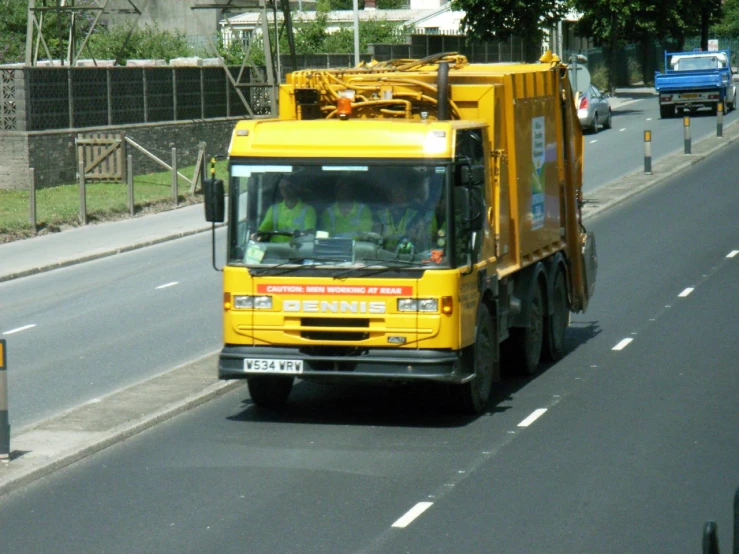 a yellow garbage truck is traveling down a street