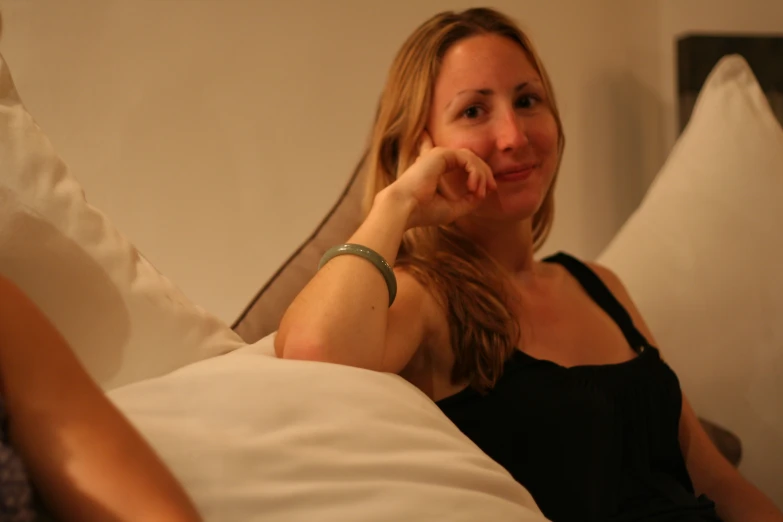 a lady lying in bed with white pillows, is smiling at the camera