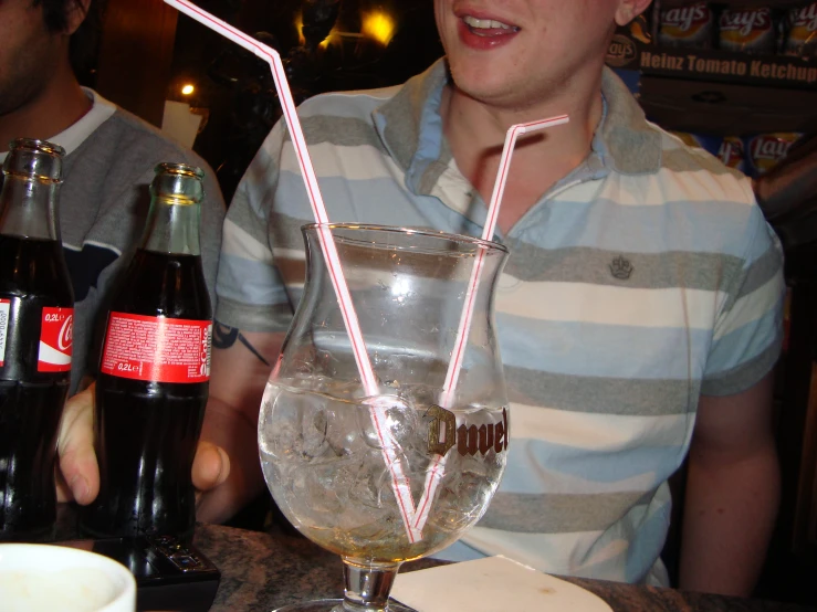 a young man sitting in front of a table with a glass and a straw in it