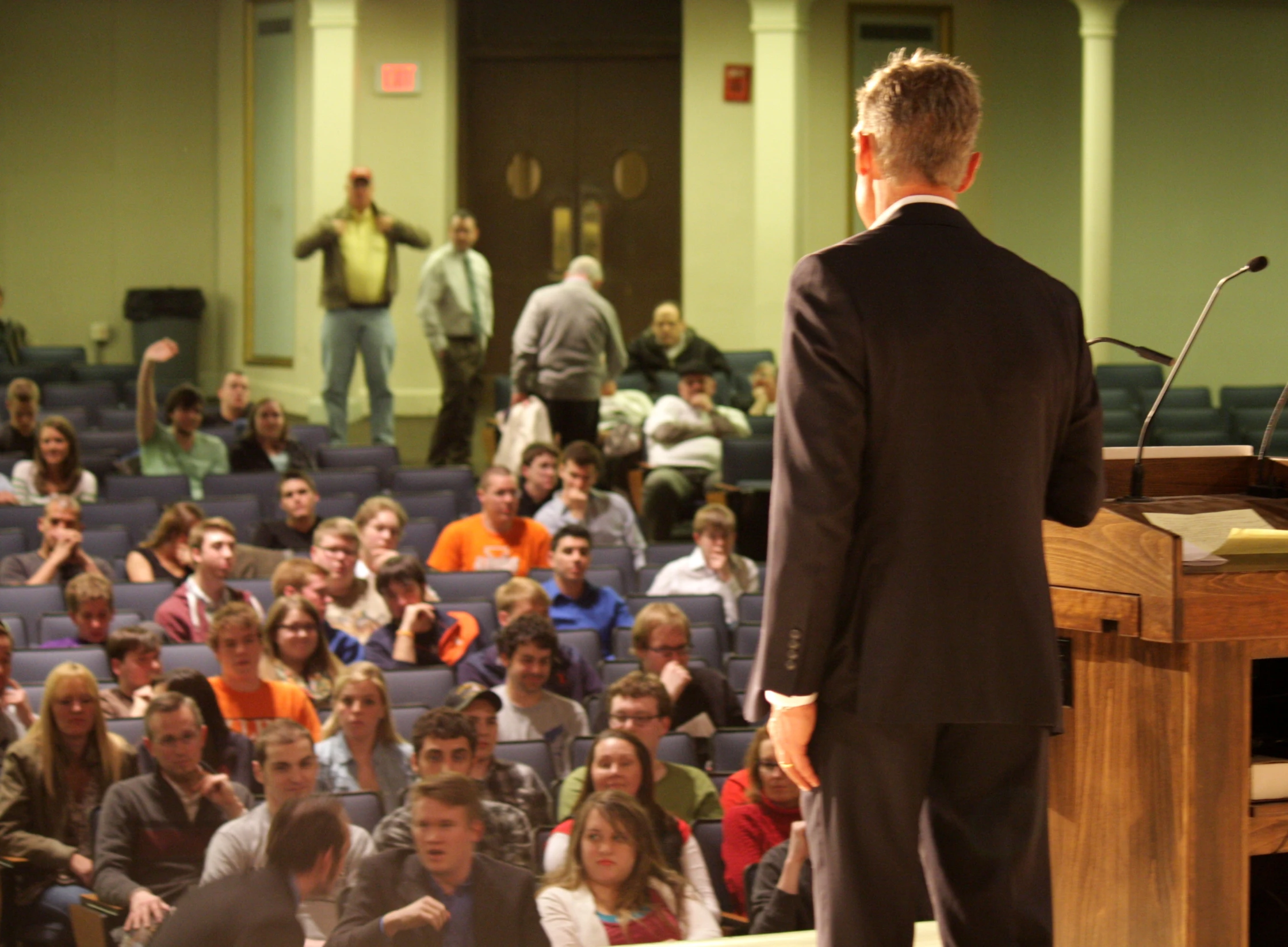 man wearing a black suit is speaking at the microphone