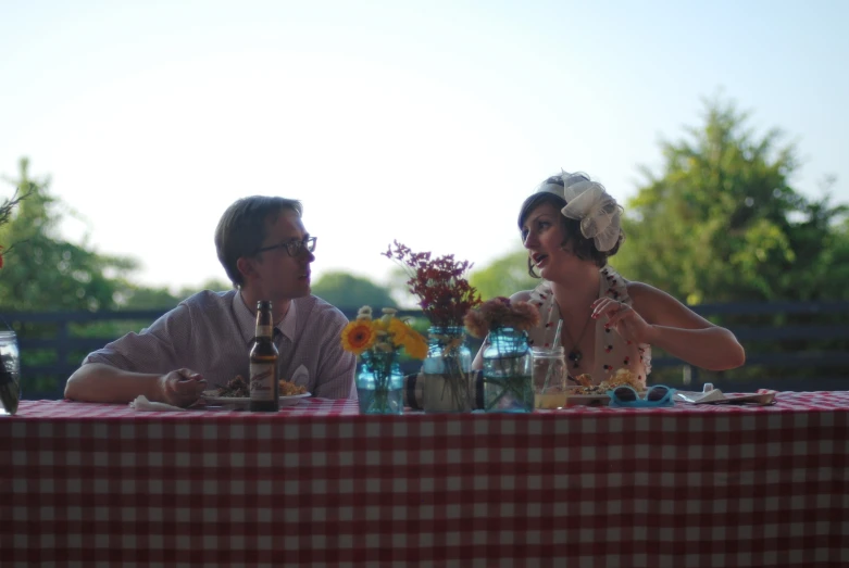 two people sitting at a table that is decorated with red and white checkered cloth