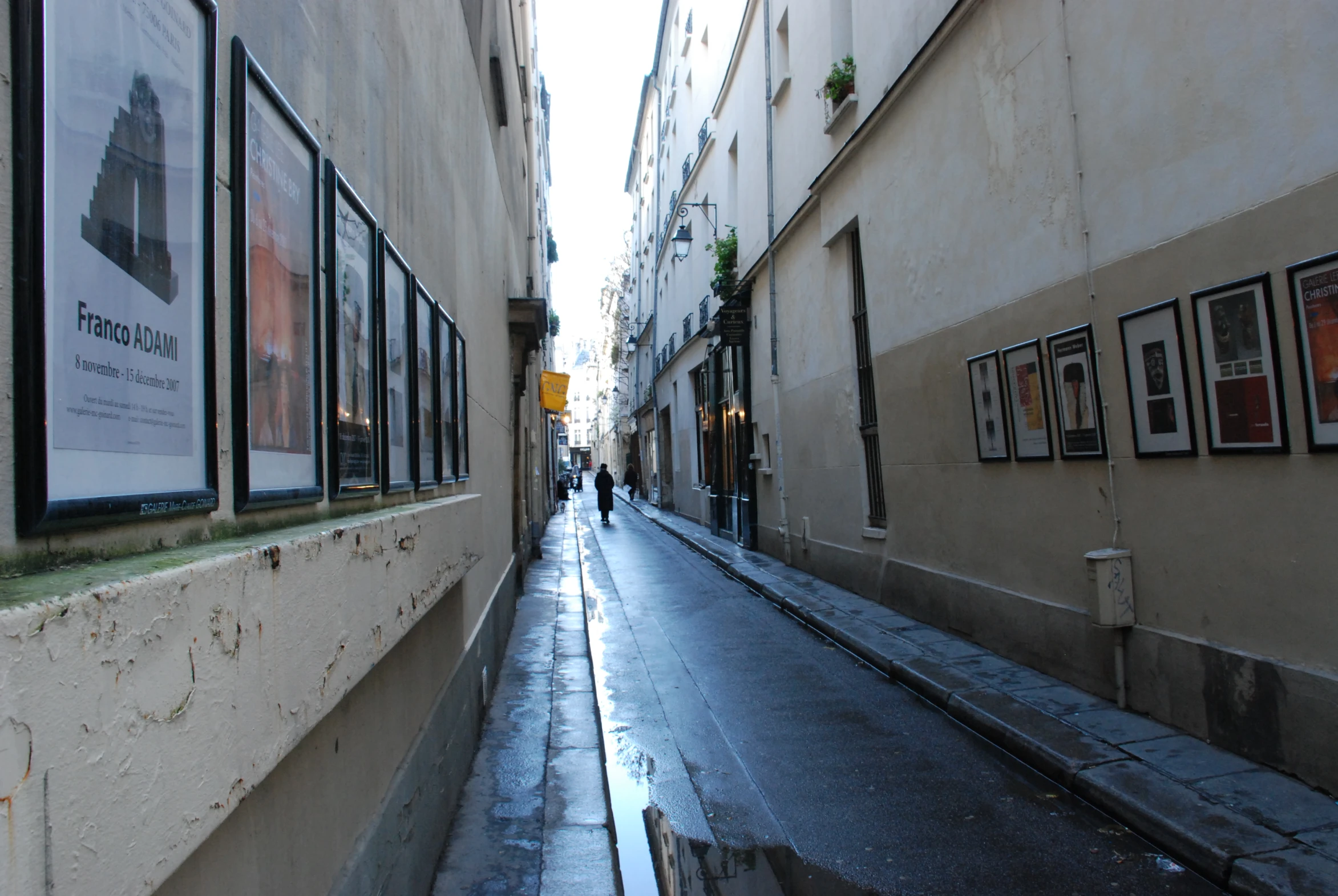 a narrow street with a few windows down one side and a wet sidewalk up the other