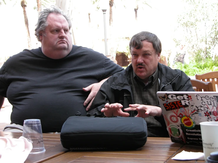 a man sitting next to a man using a laptop