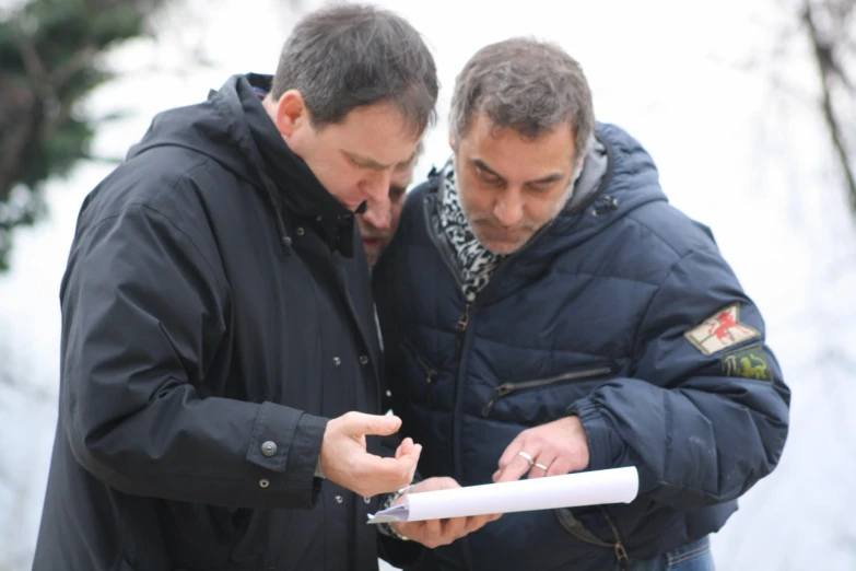 a pair of men looking at soing on a paper