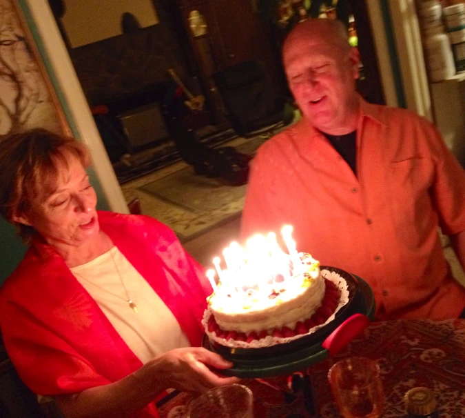 an older couple holding a birthday cake with candles on it