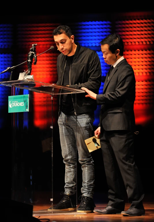 a man stands at a podium, with another man on the side