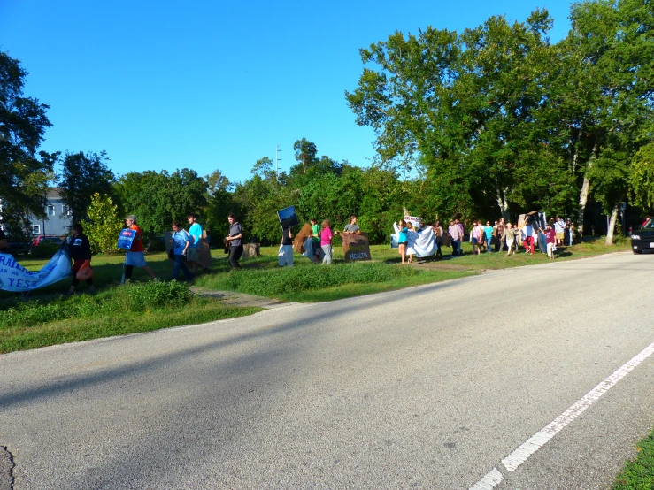 a group of people standing by a road with a car and trees