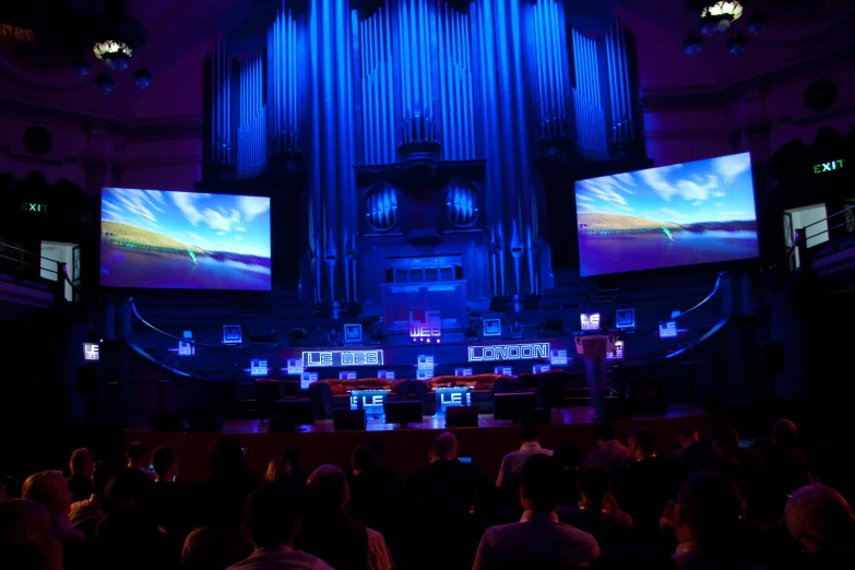 stage with people seated watching and television screens on