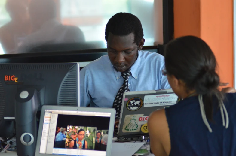 two people sitting around a computer desk looking at pictures