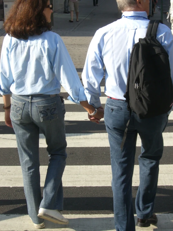 a woman holding the hand of a man as he crosses the street
