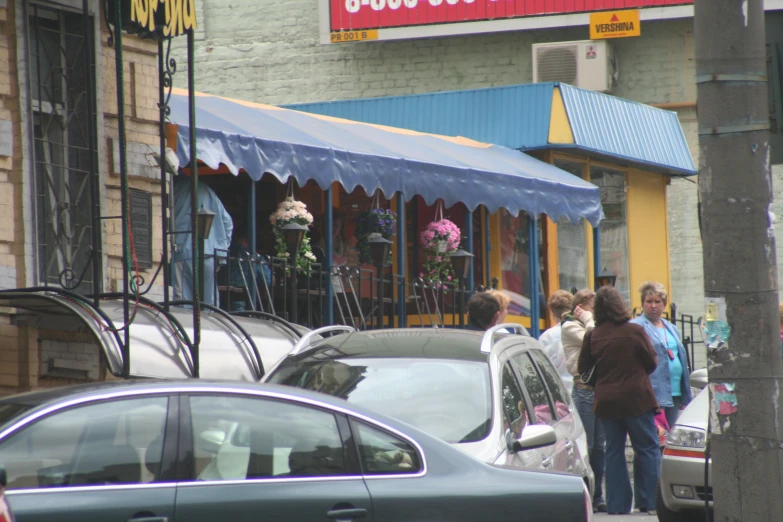 people are standing outside of a store near some parked cars