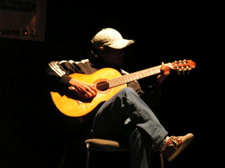 a man sitting on a chair playing an acoustic guitar