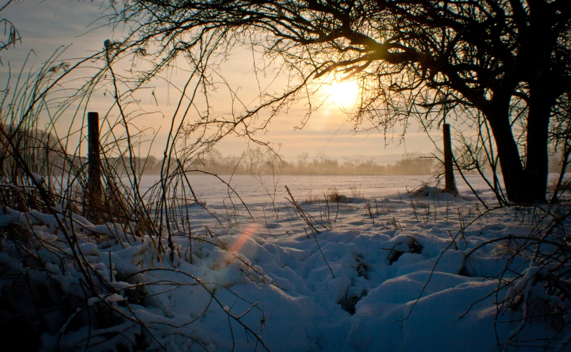 the sun is setting over the snow covered field