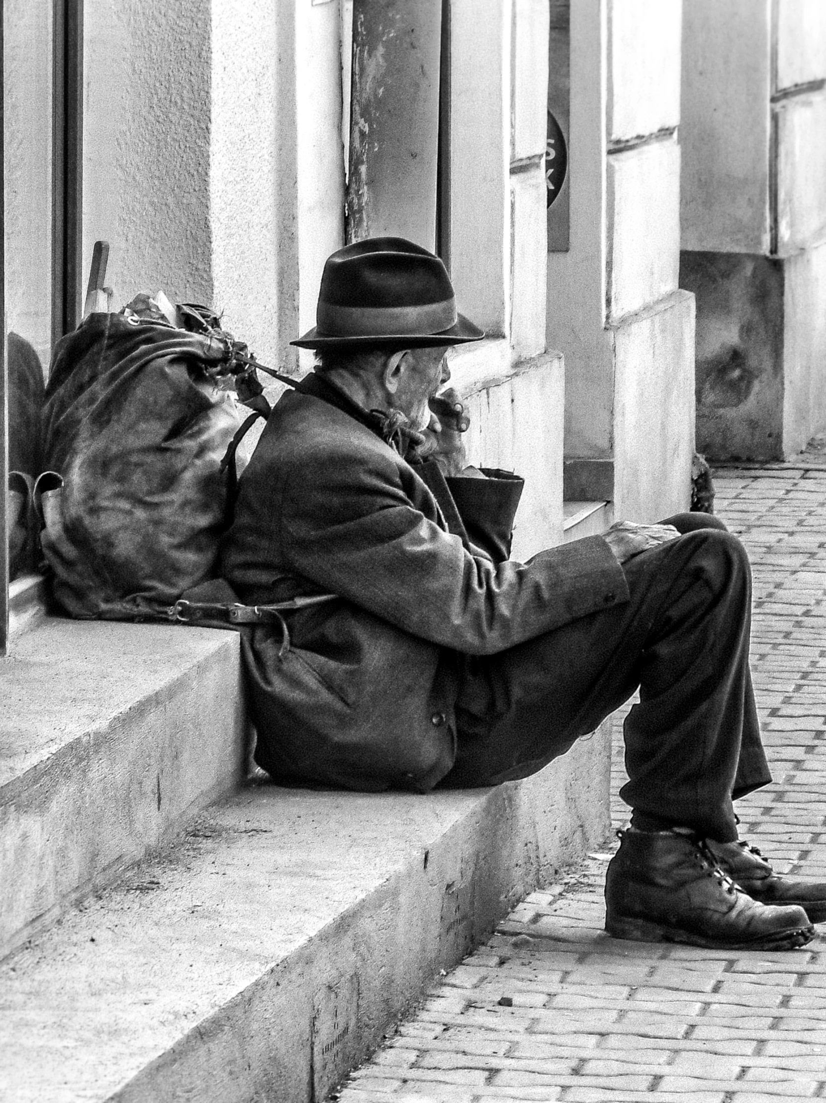 a black and white po of a man with a hat sitting on the steps looking at his phone