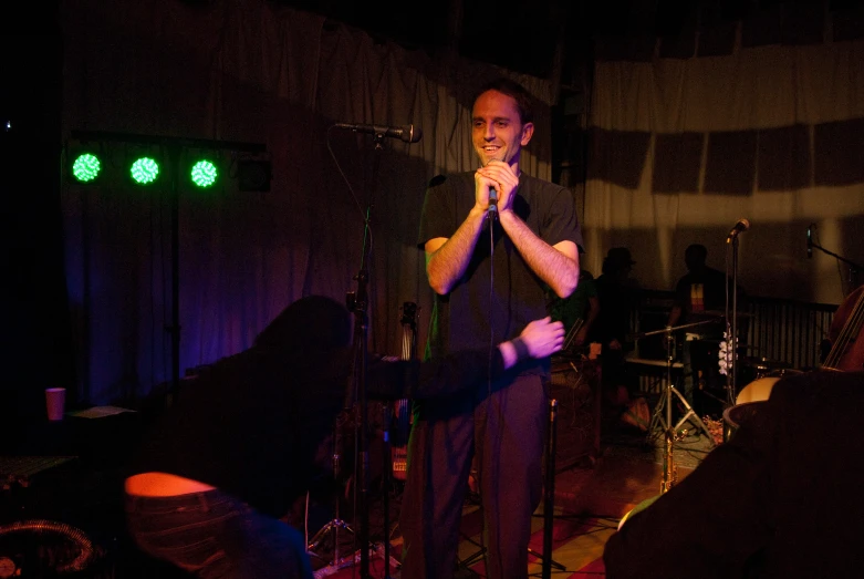 a man singing into a microphone with another band playing nearby