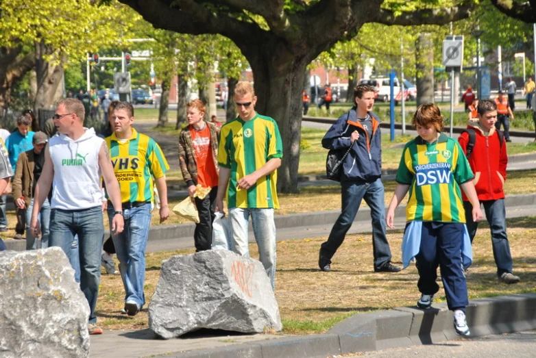 a large group of young men walk around near a big rock