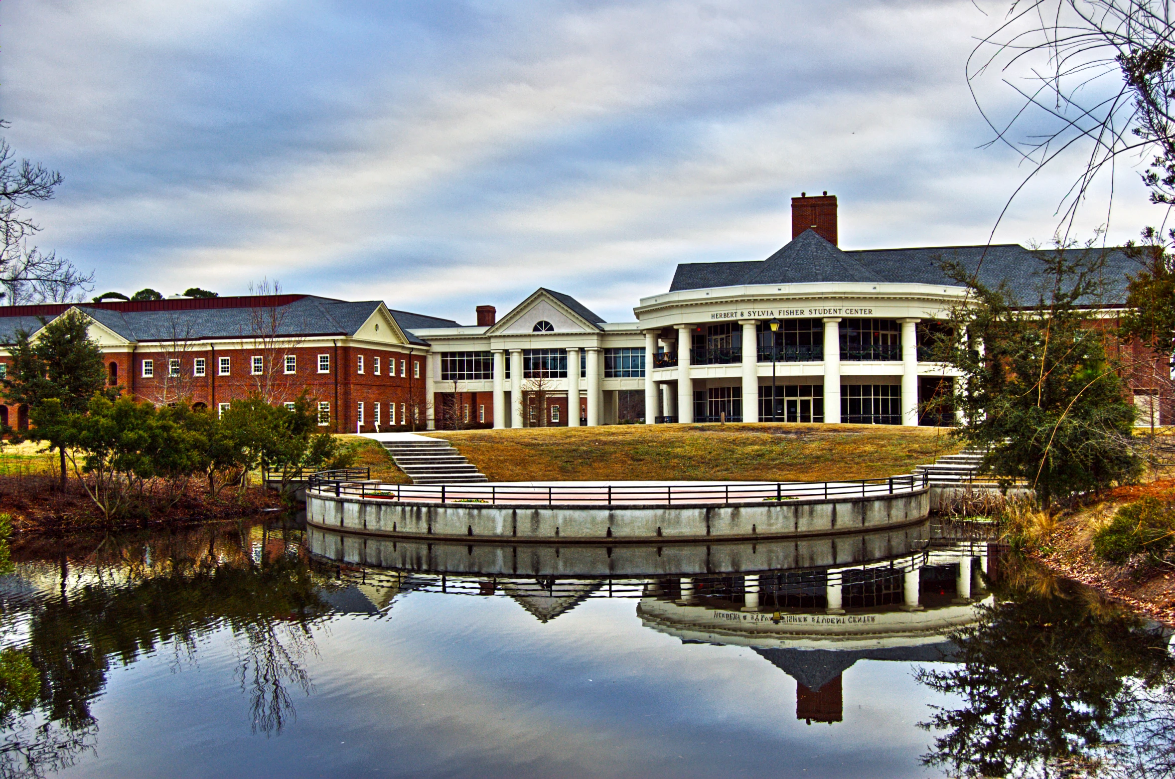 an old brick building by a pond with trees and plants around it