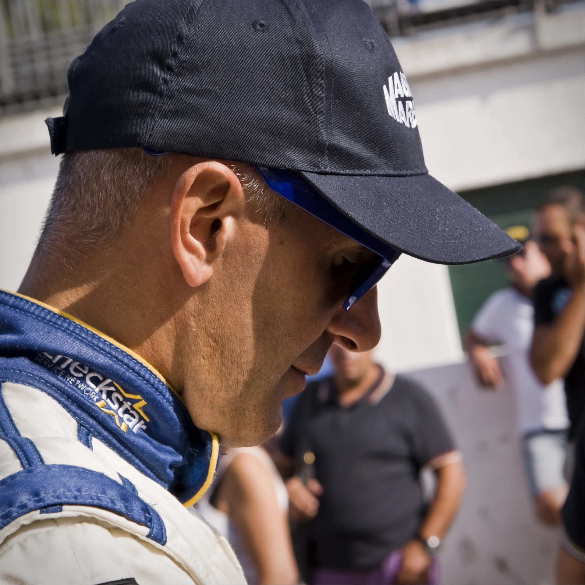 man in a racing outfit holding a cell phone while other people talk on their cell phones