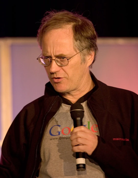 man with black glasses and grey jacket holding up a microphone