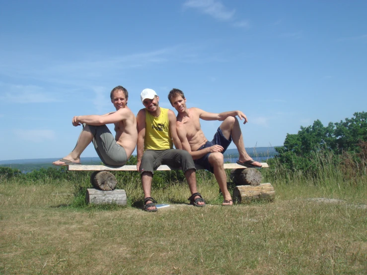 three men hanging out on a bench in a field