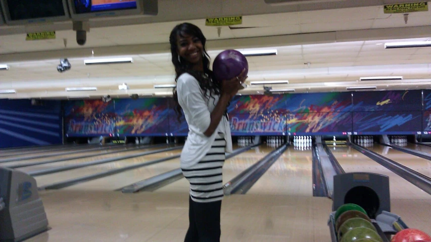 a woman smiles and poses with her bowling ball