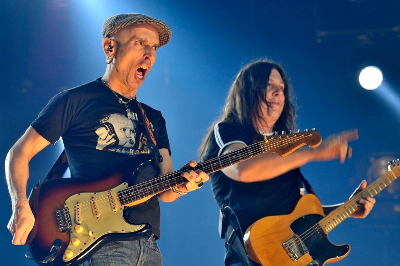 two people with guitars stand in front of a spotlight