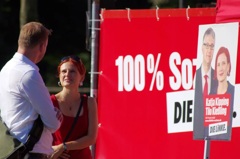 man and woman standing next to a political billboard