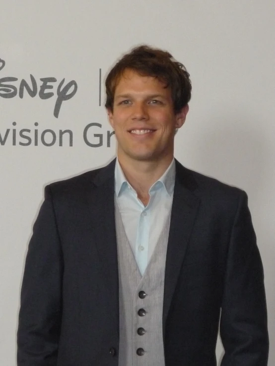 a man in black jacket and vest standing in front of a disney logo