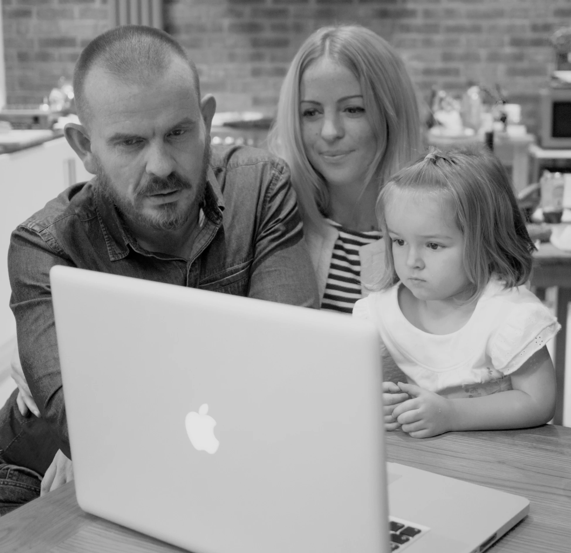 two adults and one child are looking at a laptop
