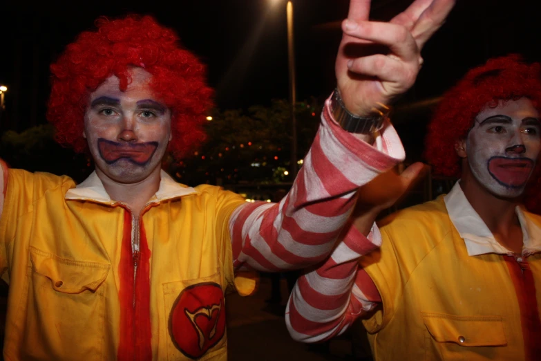 three clowns dressed up with red hair and makeup giving the peace sign