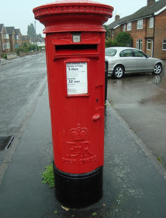 a red and black post box some cars and a street