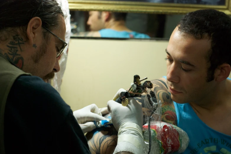 a man getting his arm tattoo while holding a camera