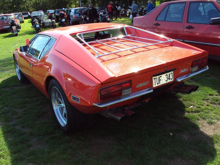 an orange and red sports car parked on top of a lush green field