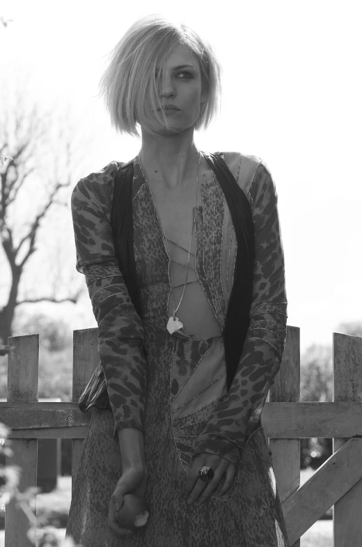 a person with short hair posing by a fence